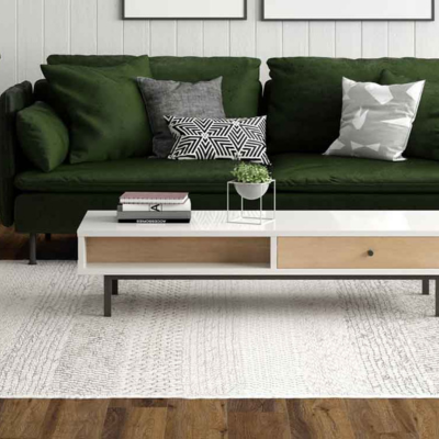 Green couch with wood look floors and white coffee table matching the white patterned area rug.